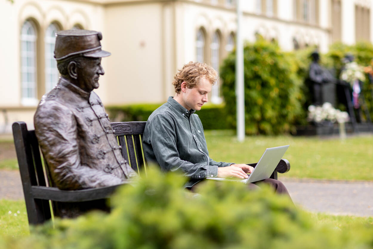 Geels werkt via de laptop op een bankje voor het voormalige paleis
