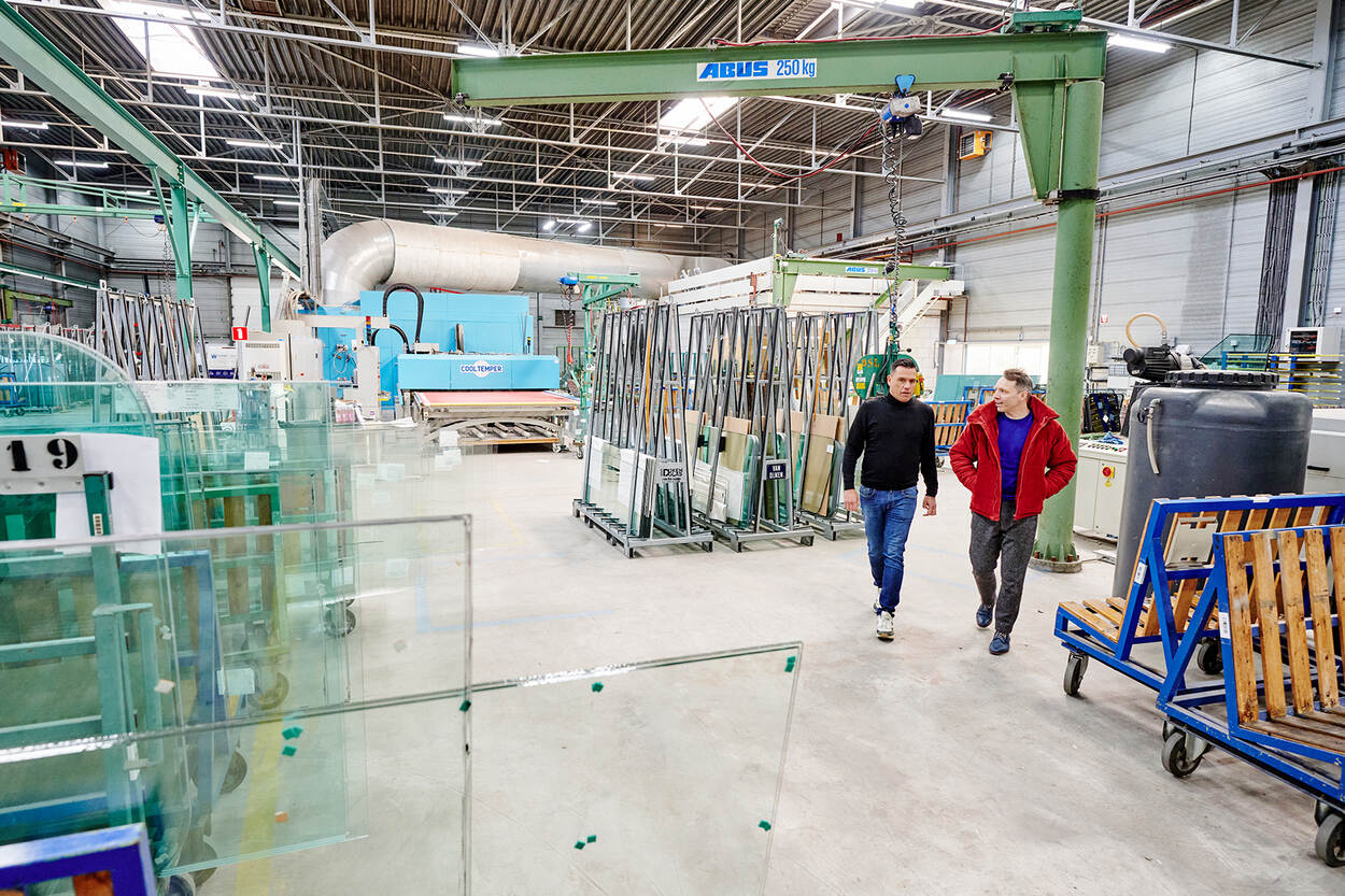 Jor Zacharias (links) en Rutger Snoek (rechts) lopen tussen apparatuur van een glasfabriek.