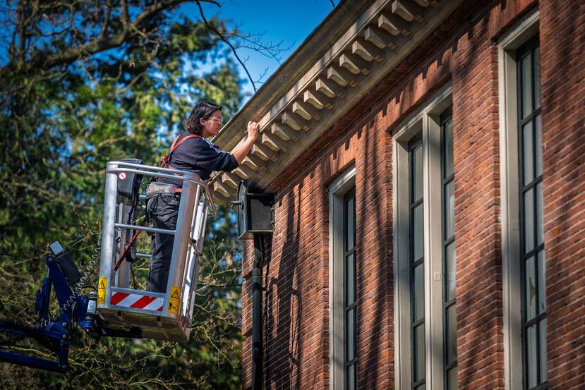 Lynn van Rijnsover doet kleurhistorisch onderzoek aan de gevel van Villa Den Engh vanuit een hoogwerker.